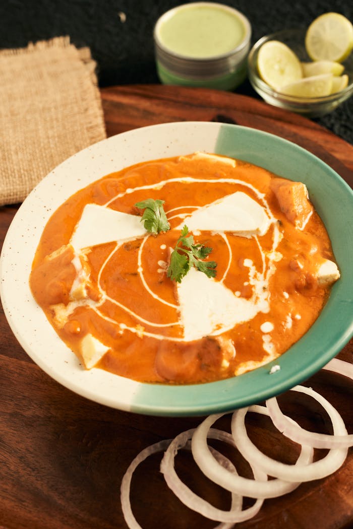 Creamy paneer makhani served in a bowl with onion rings and garnished with fresh herbs.