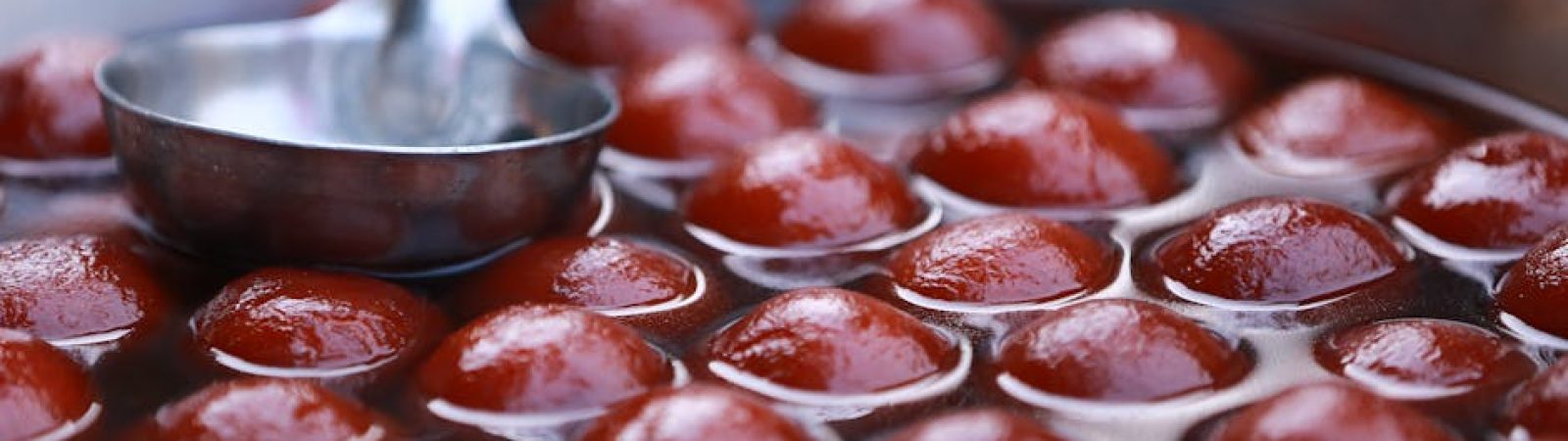Close-up view of Gulab Jamun in a stainless steel pot, popular Indian dessert street food.